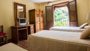Un dormitorio con dos camas, un escritorio de madera con una computadora, una silla y una ventana con vista a la vegetación.