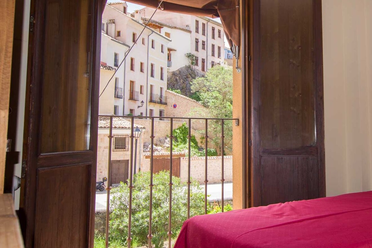 A room with a bed, a wooden headboard, and a view of buildings through an open door.