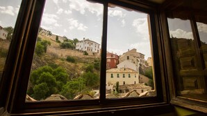 Vista a través de una ventana con muros y puente de piedra, con vistas a una colina con edificios.