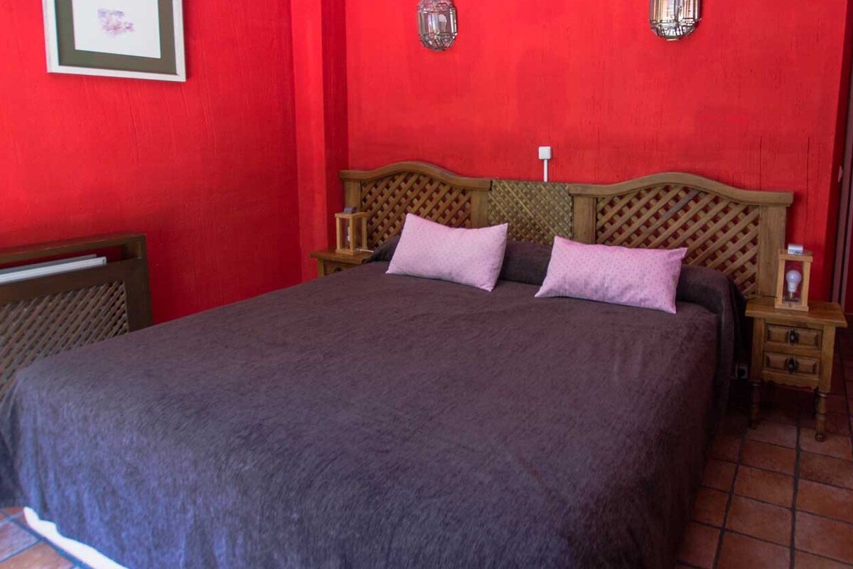 A room with a large bed, wooden headboard, two bedside tables, and a red wall.