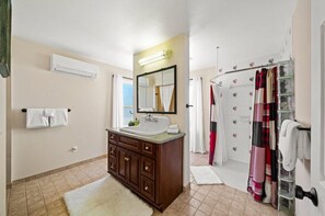 A bathroom with a wooden vanity, a large mirror, a shower with a glass door, and a towel rack. - Charming, Hill Country Small-town Suite, Centrally located. (Harper)