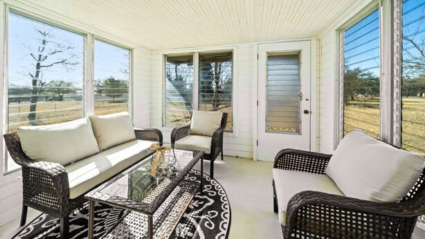 A sunroom with wicker furniture, large windows, and a patterned rug. - Charming, Hill Country Small-town Suite, Centrally located. (Harper)