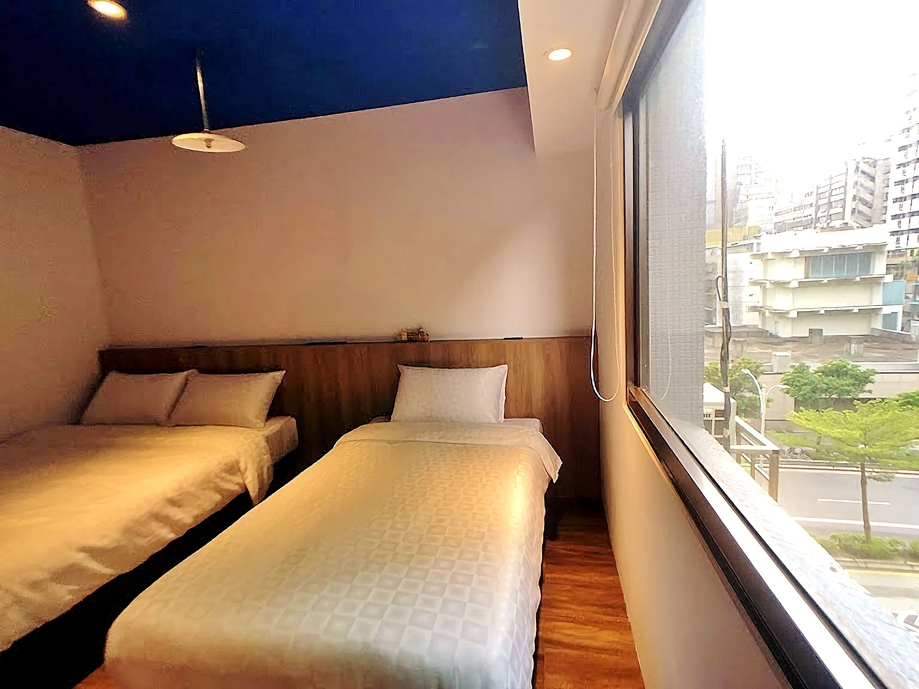 Hotellihuone, jossa on kaksi erillistä sänkyä, puinen pääty, kattovalaisin ja ikkuna, josta avautuu näkymä kaupunkiin.