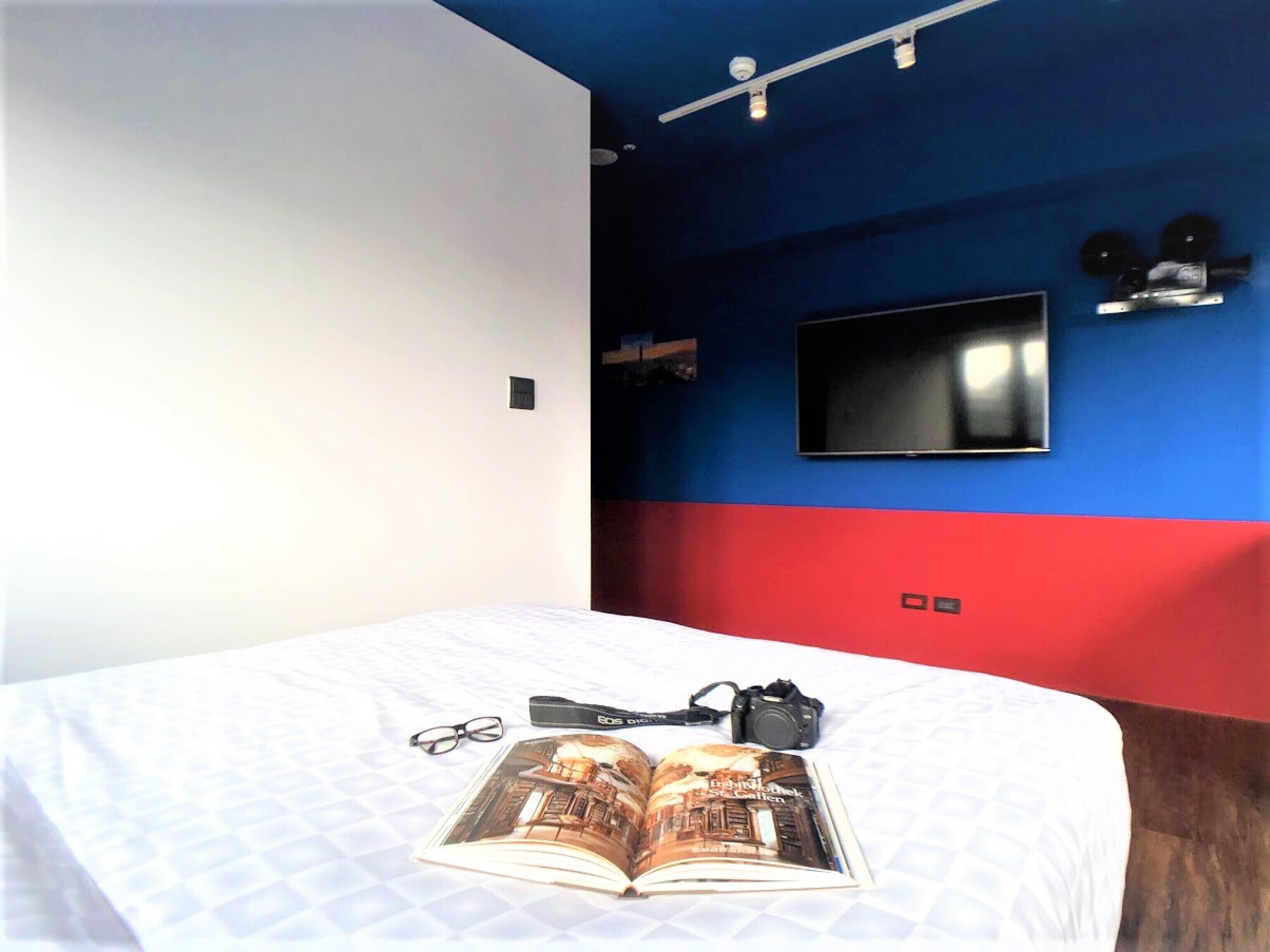 A bedroom with a bed, a book, glasses, and a camera on the bed.
