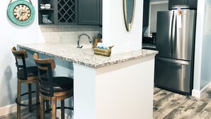 A kitchen with dark cabinets, a stainless steel refrigerator, a granite countertop, and two bar stools.