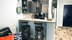 A kitchen with bar stools, a clock, and a coffee maker.