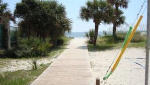 A wooden boardwalk leading to a beach with palm trees and a clear sky.