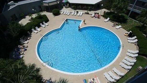 A circular swimming pool surrounded by lounge chairs and a covered area.
