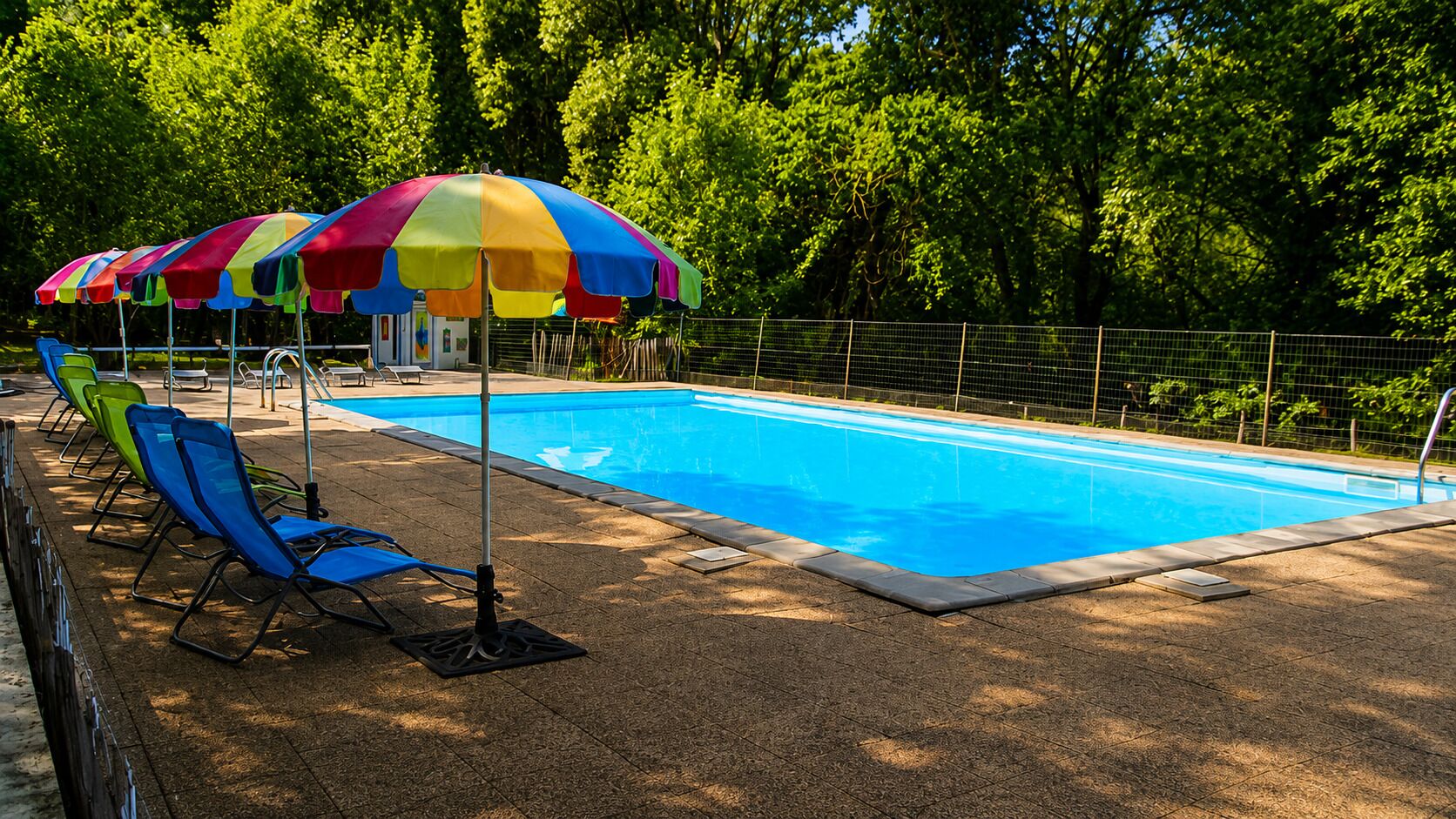 Una piscina amb gandules i ombrel·les, envoltada per una tanca i arbres.