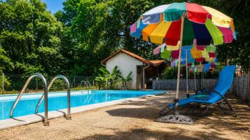 A swimming pool with a metal ladder, a colorful umbrella, and a blue lounge chair.
