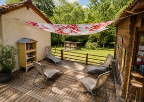A wooden deck with metal chairs, a bookshelf, and a small wooden structure in the background.