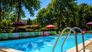 Une piscine avec un escalier en métal, des chaises longues vertes et roses, et des parasols rouges.