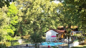 Ein Poolbereich mit umzäuntem Deck, einer kleinen Gartenhütte und Sonnenschirmen.