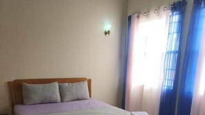 Een slaapkamer met een bed, nachtkastje, wandlamp en raam met gordijnen.