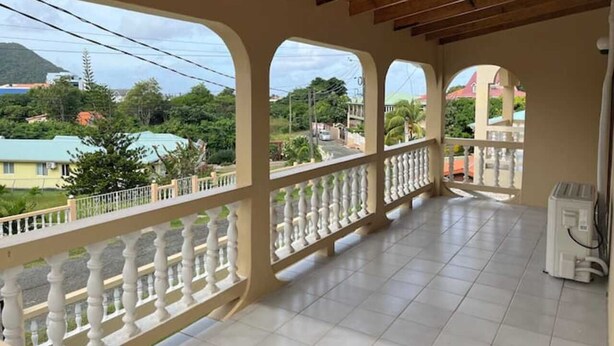 Een overdekt balkon met witte balustrades, een betegelde vloer en uitzicht op een woonwijk met huizen en groen.