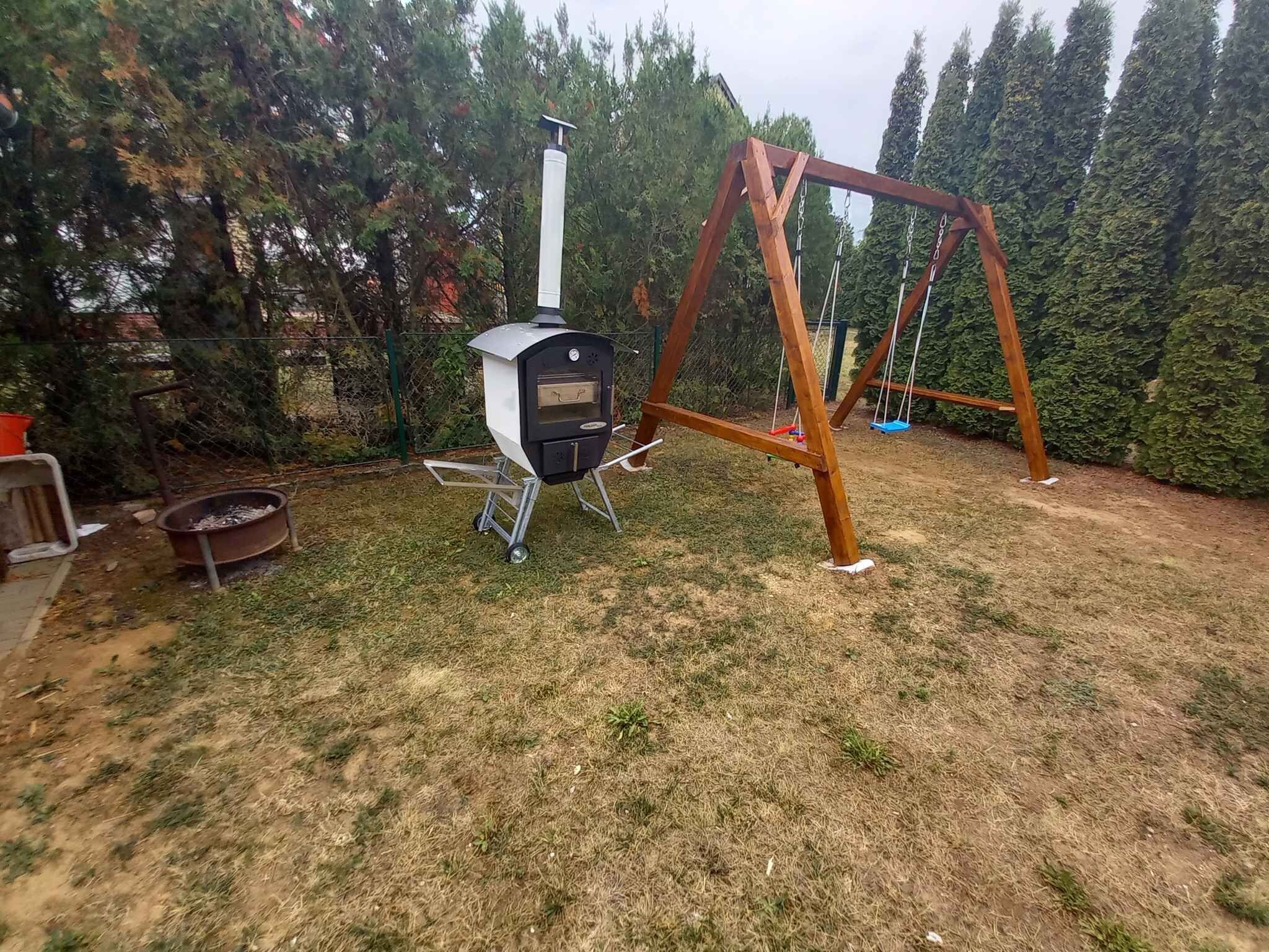 A backyard with a wood-burning stove, a swing set, and a fenced area.