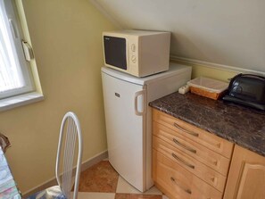 A compact kitchenette with a refrigerator, a microwave, a toaster, and a chair.
