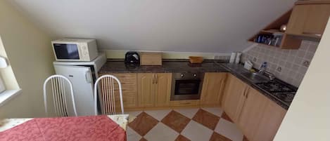 Une cuisine de taille réduite équipée d’un four à micro-ondes, d’une cuisinière et de meubles de rangement simples.
