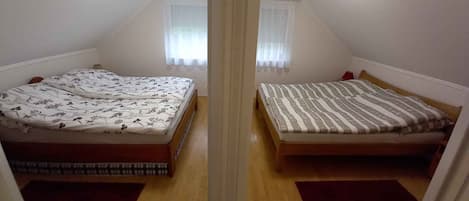 A mirrored room with two beds, a window with curtains, and a ceiling light.