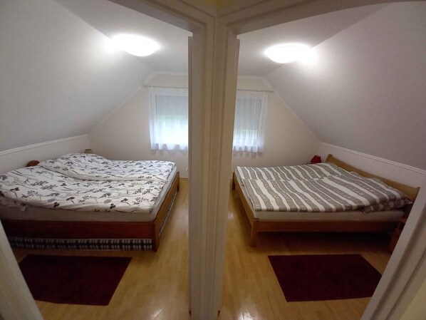 A mirrored room with two beds, a window with curtains, and a ceiling light.