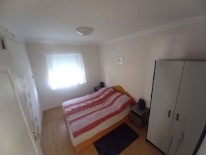 A bedroom with a bed, a wardrobe, a nightstand, a window with curtains, and a door.