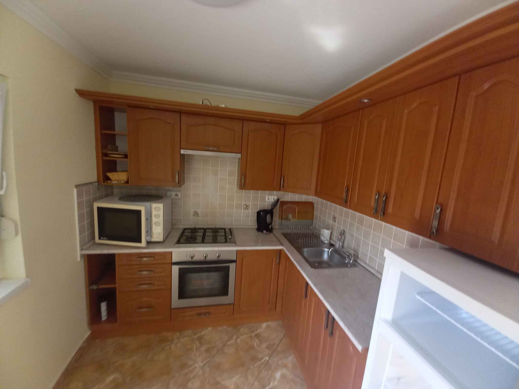 A compact kitchen with wooden cabinets, a microwave, stove, oven, and a sink.