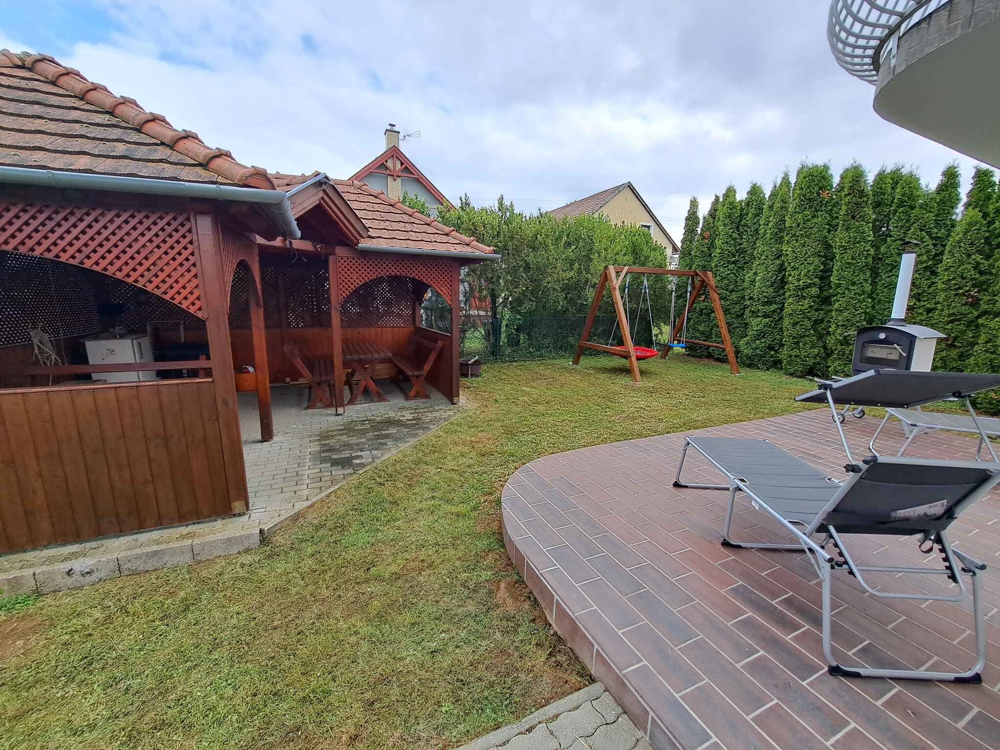 A backyard with a wooden pergola, a swing set, a barbecue grill, and a brick patio.