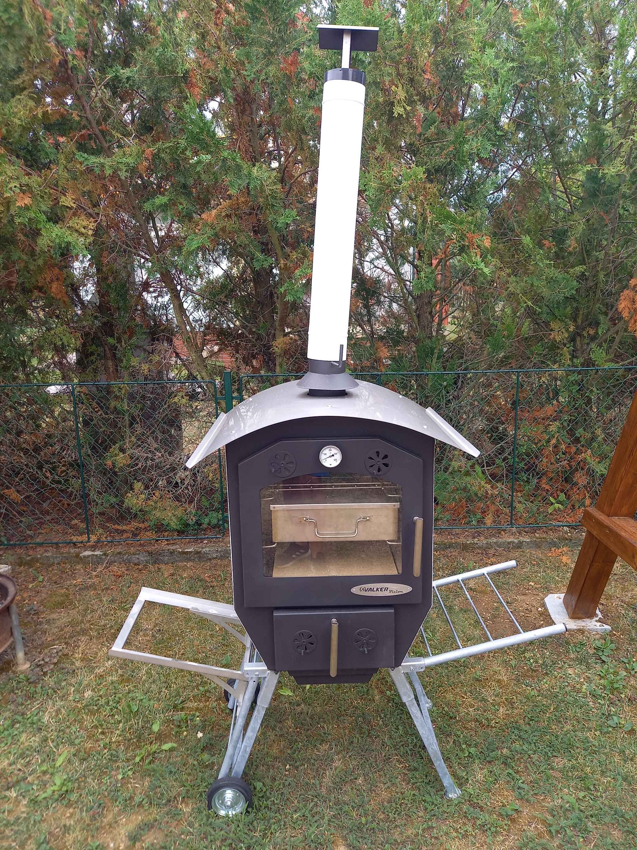 An outdoor wood-burning stove with a chimney, a thermometer, and a metal rack for holding items.