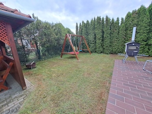 A backyard with a swing set, a brick patio, and a wood-burning stove.
