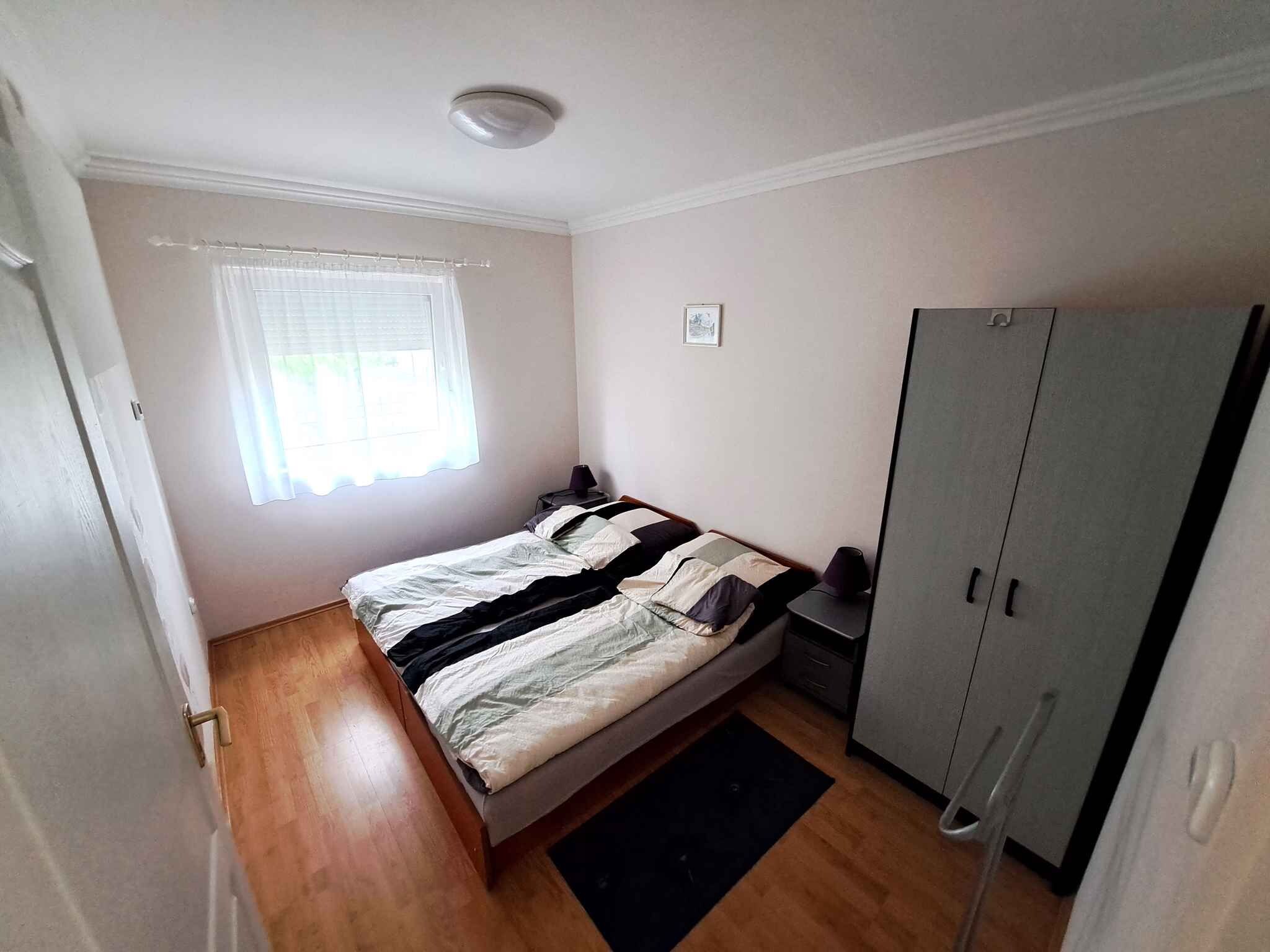 A bedroom with a bed, a wardrobe, a nightstand, a lamp, and a window with curtains.