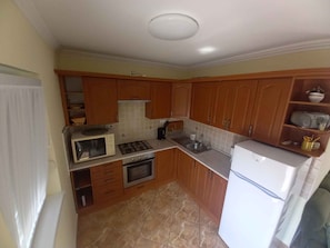 A compact kitchen with wooden cabinets, a gas stove, a microwave, a sink, and a refrigerator.
