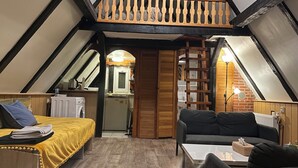Ein gemütliches Schlafzimmer im Dachgeschoss mit einem Bett, einer Couch und einem kleinen Tisch. Es gibt eine Küchenzeile mit Spüle und Herd. Der Raum verfügt über Holzbalken und eine geneigte Decke.