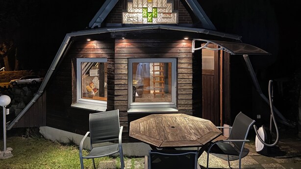 Eine Holzhütte mit einem Satteldach, großen Fenstern und einem Essbereich mit Tisch und Stühlen.