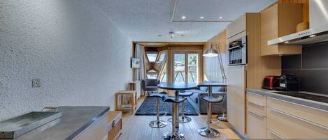 A modern kitchen with a central island, bar stools, and a view of the outdoors.