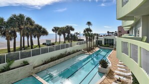 A pool area with multiple swimming lanes, palm trees, and a view of the beach. - Ocean Grove 704-Ocean View by Ryson Vacation Rentals (Galveston)