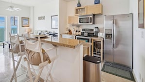 A modern kitchen with a central island, stainless steel appliances, and a view to the outside. - Ocean Grove 704-Ocean View by Ryson Vacation Rentals (Galveston)