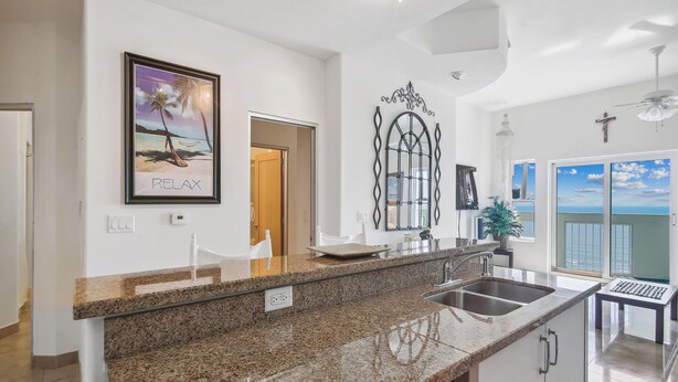 A modern kitchen with granite countertops, stainless steel appliances, and a view of the ocean through large sliding doors. - Ocean Grove 704-Ocean View by Ryson Vacation Rentals (Galveston)