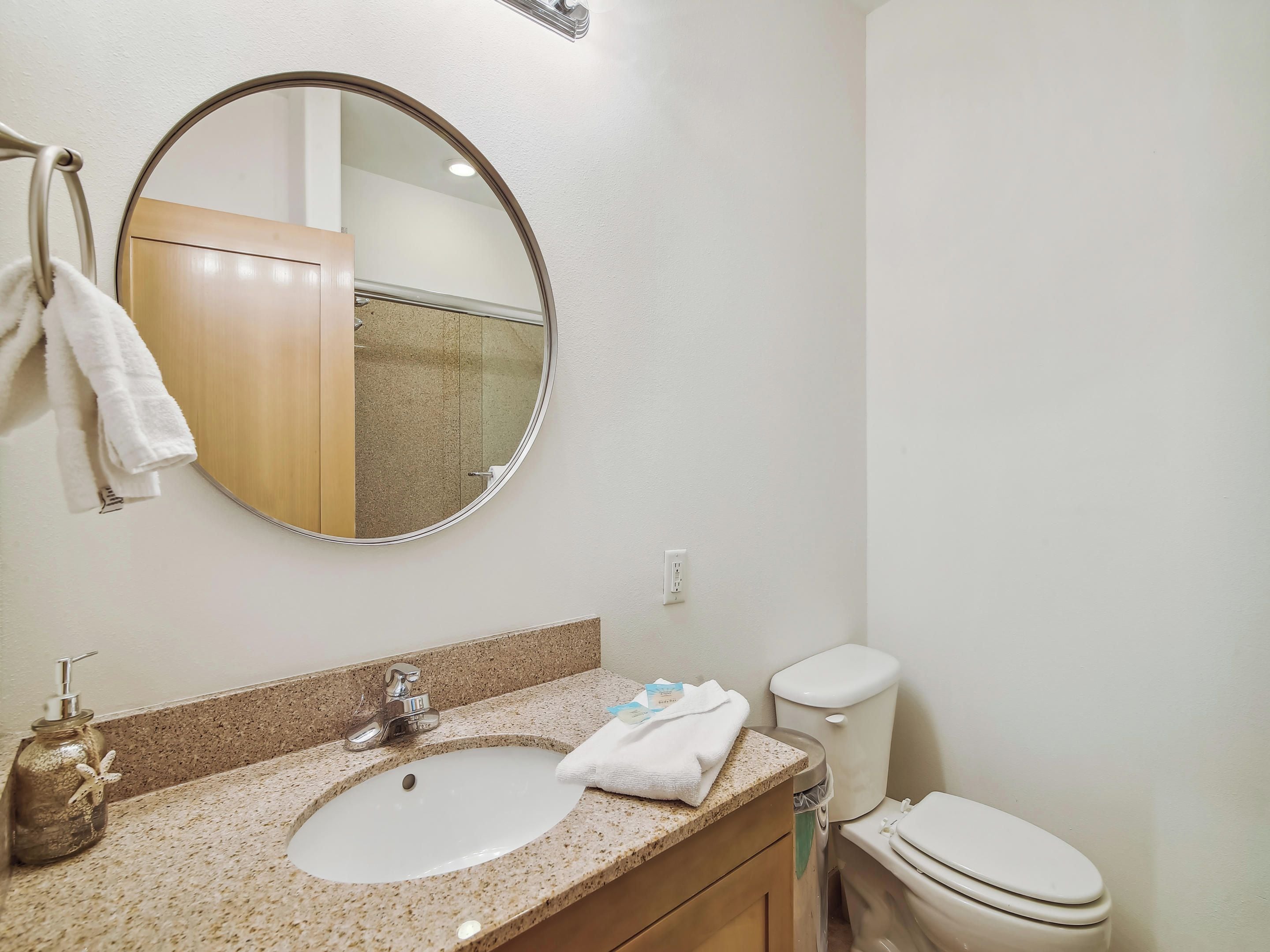 Une salle de bain avec un miroir rond, un lavabo, des toilettes et un porte-serviettes.