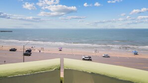 A coastal road with a beach in the background, a pier extending into the sea, and a clear sky with scattered clouds. - Ocean Grove 704-Ocean View by Ryson Vacation Rentals (Galveston)