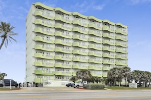 A multi-story hotel with balconies, a parking area, and palm trees.