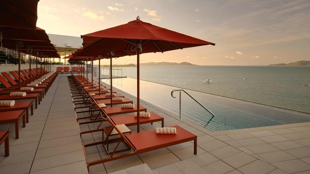 A poolside area with sun loungers and umbrellas, overlooking a calm sea with boats. - Ardo (Townsville)