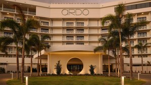 A multi-story hotel with the name "ORDO" prominently displayed on the facade. It features balconies on each floor, a central archway entrance, and is surrounded by palm trees. - Ardo (Townsville)