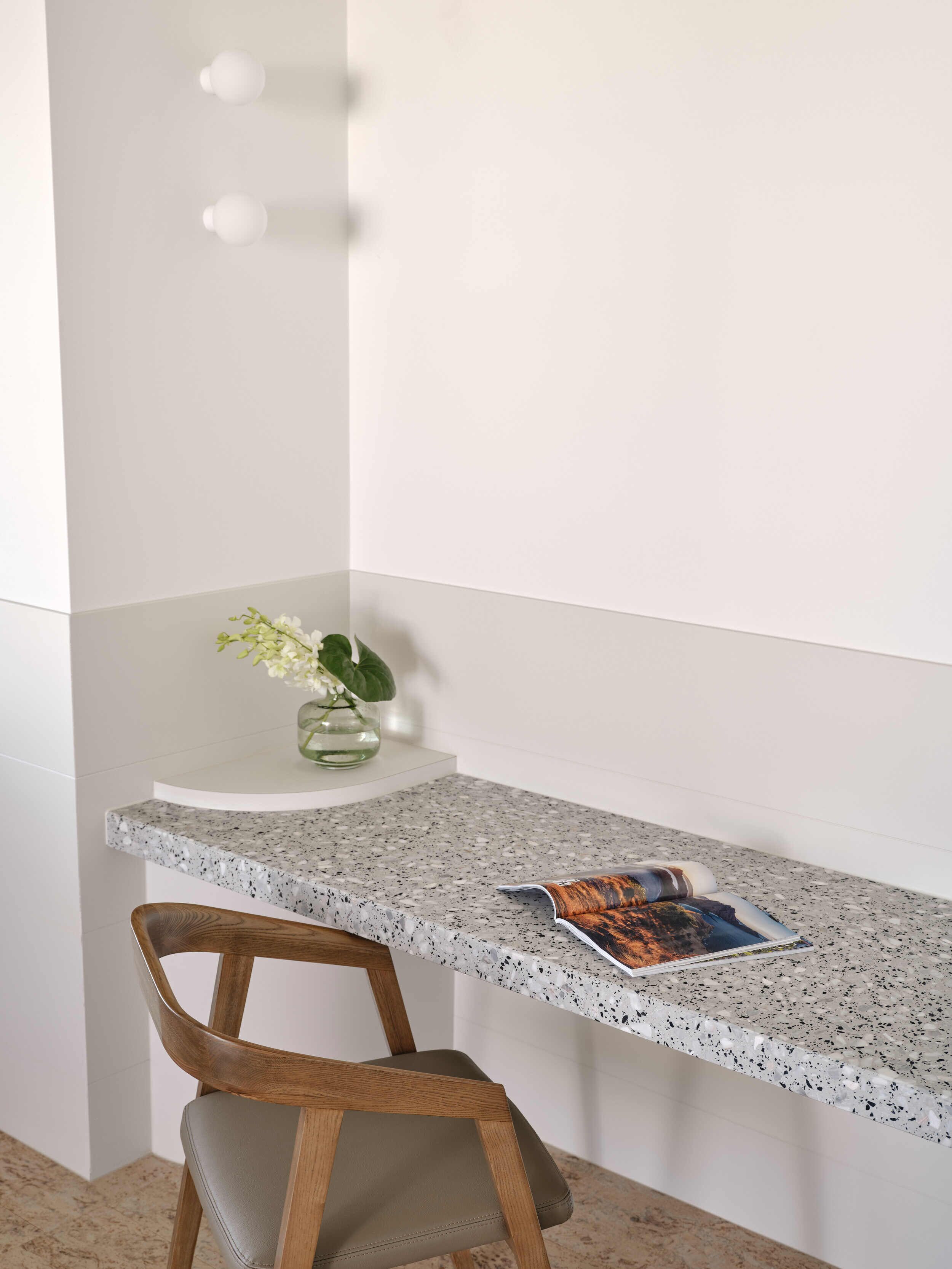 A corner desk with a speckled countertop, a wooden chair, and a vase with flowers.