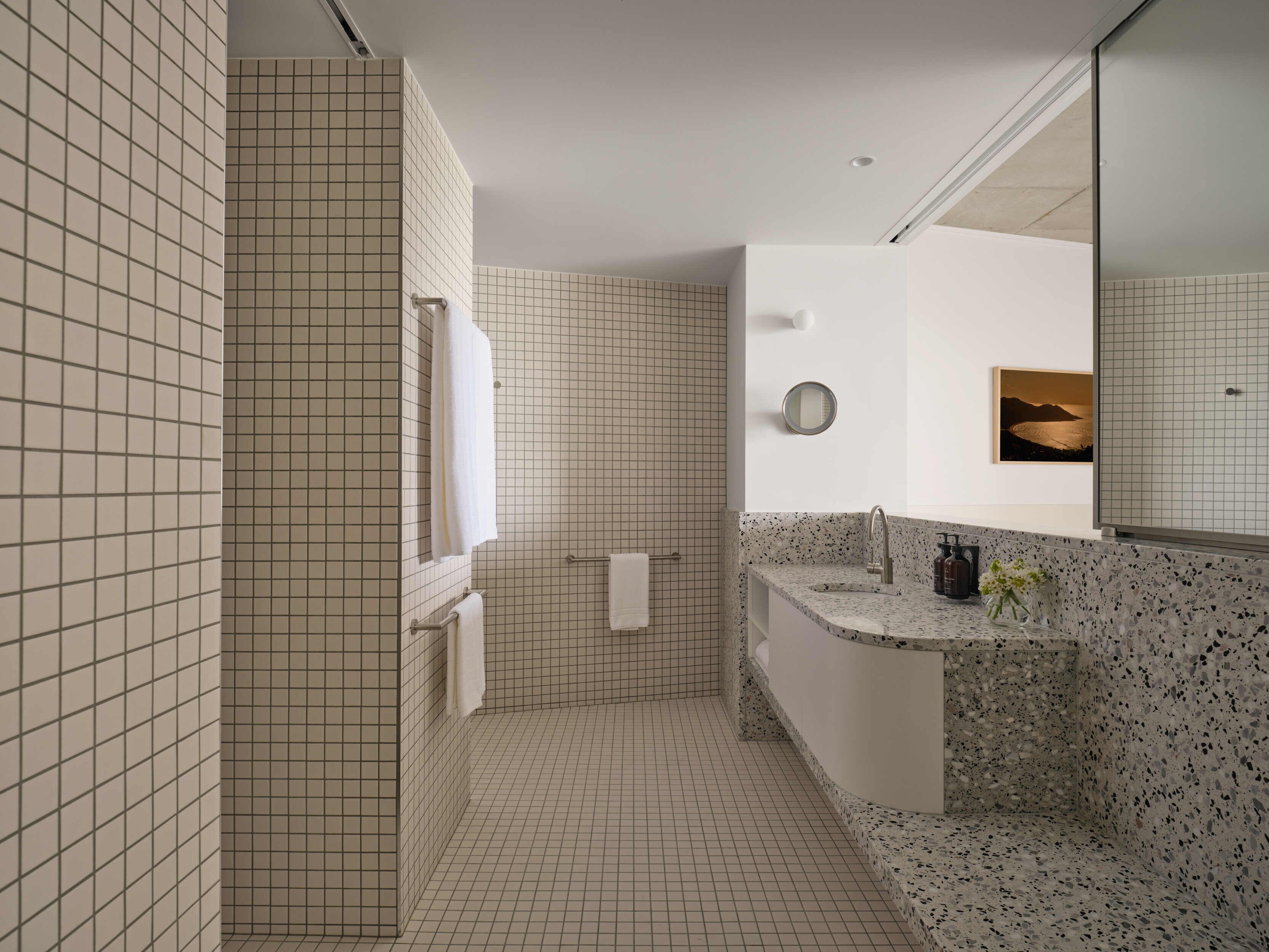 A modern bathroom with a tiled shower, a sink with a speckled countertop, and a large mirror.