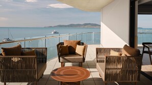 A balcony with wicker furniture, a glass railing, and a view of the sea with boats. - Ardo (Townsville)