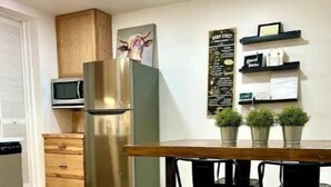 A modern kitchen with a stainless steel refrigerator, wooden cabinets, a microwave, and a dining area with black chairs. - South Side Bicycle Home Sleeps 6 (Pittsburgh)