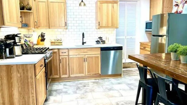 A modern kitchen with wooden cabinets, a stainless steel dishwasher, and a bar area with stools. - South Side Bicycle Home Sleeps 6 (Pittsburgh)