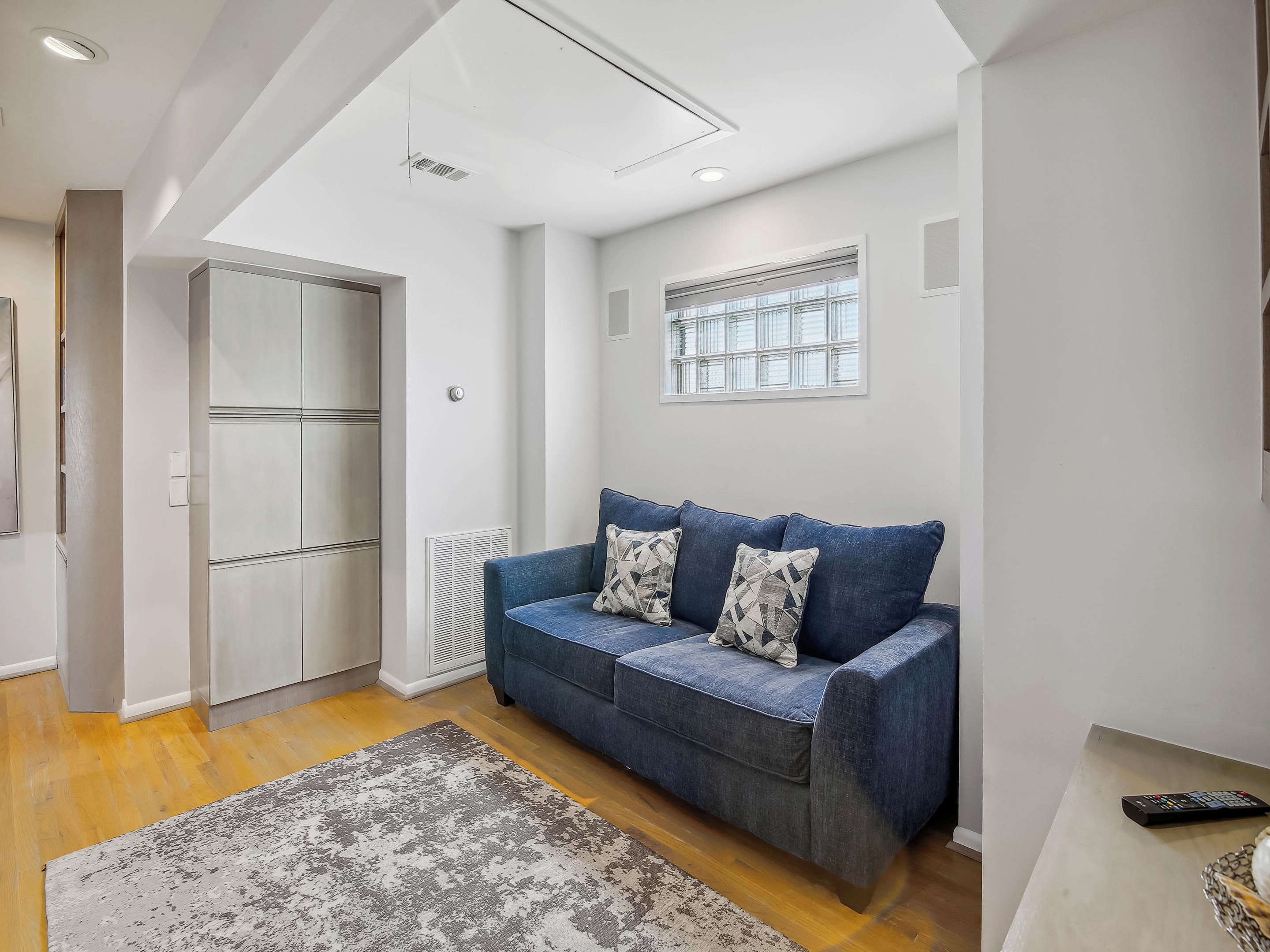 A modern living room with a blue sofa, a patterned rug, and a window with blinds.