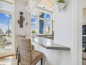 A modern kitchen with a large window, a bar area, and wicker chairs. - Pirates' Castle by Ryson Vacation Rentals (Galveston)