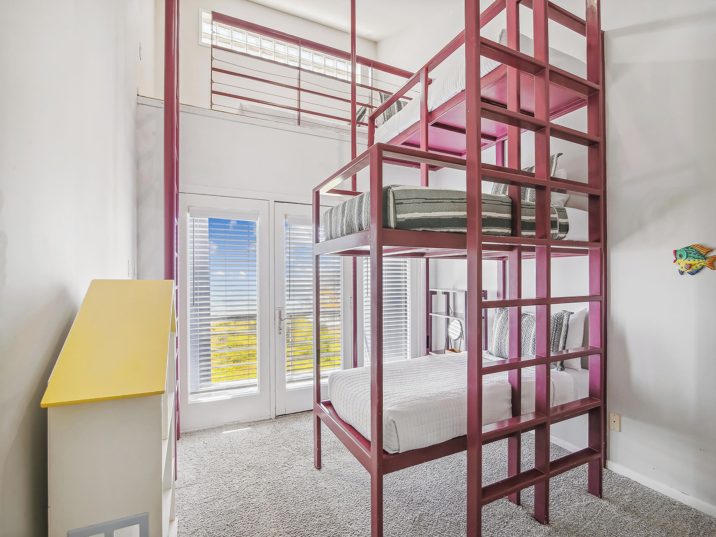 A room with a bunk bed, a yellow desk, and a window with blinds.